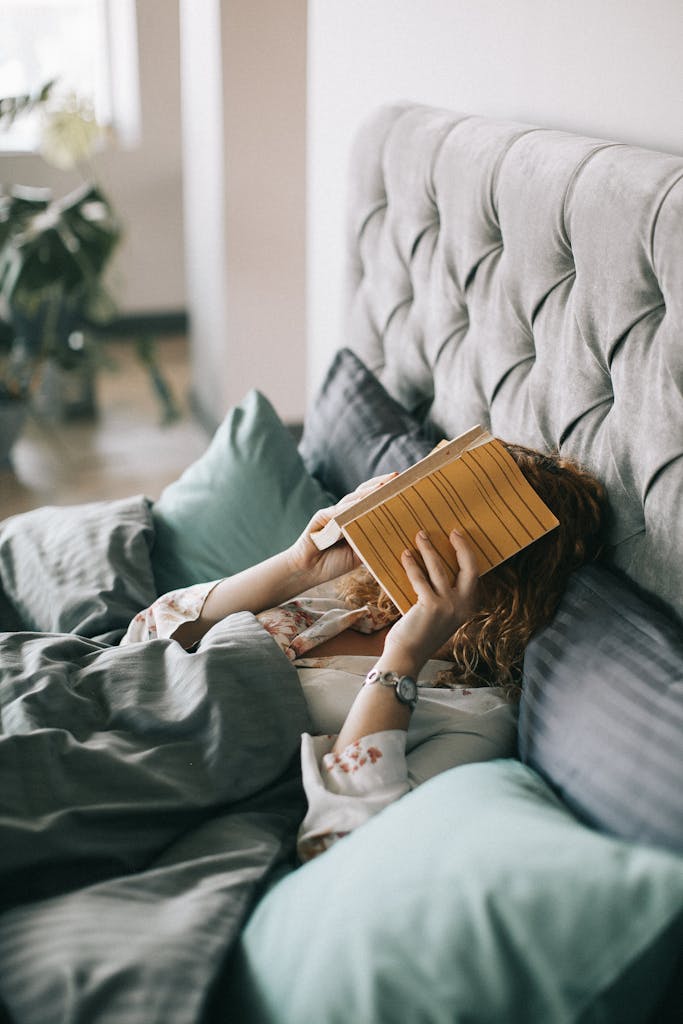 Woman resting in bed holding a book, creating a serene indoor atmosphere perfect for relaxation and leisure.